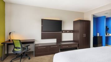 A hotel room with a bed, a desk with a chair, a TV mounted on the wall, and a wardrobe.