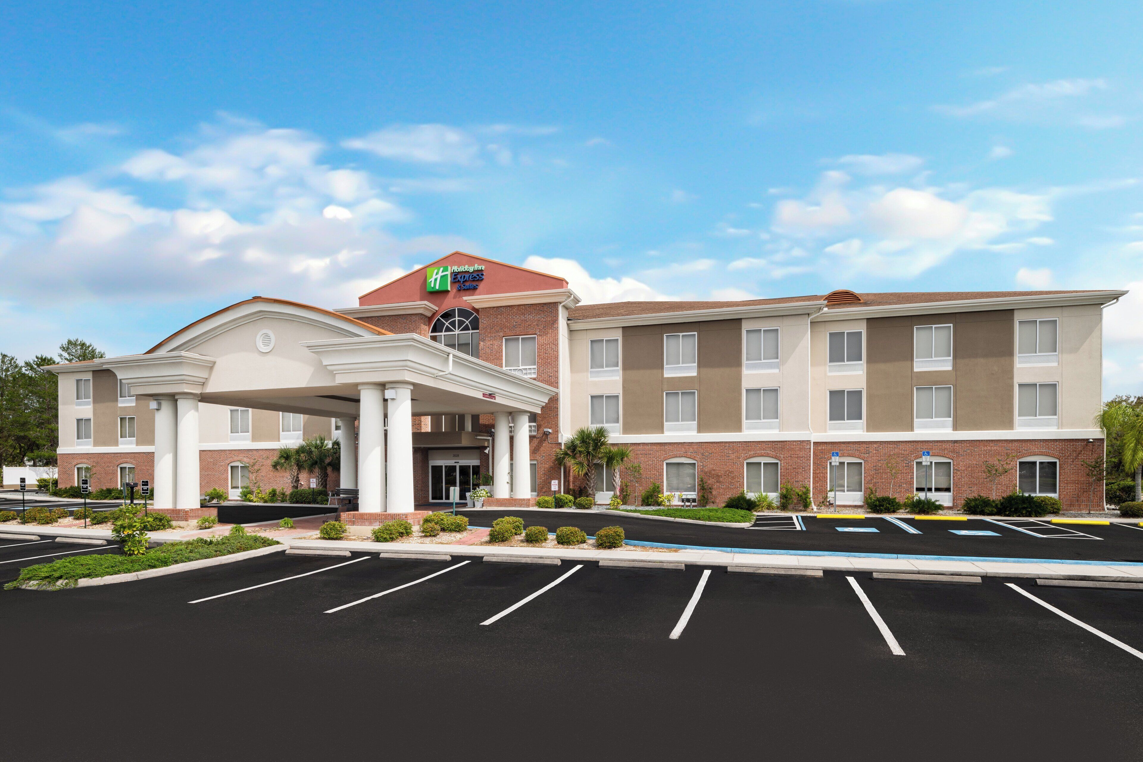A multi-story hotel with a central entrance, parking lot, and landscaped surroundings.