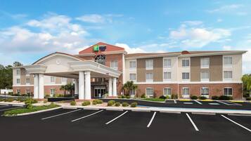 A multi-story hotel with a central entrance, parking lot, and landscaped surroundings.