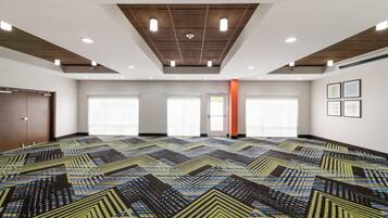 Una amplia sala de conferencias con alfombra estampada, luces empotradas en el techo y grandes ventanales.