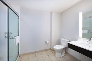 A modern bathroom with a glass shower enclosure, a white toilet, and a black countertop with a mirror.