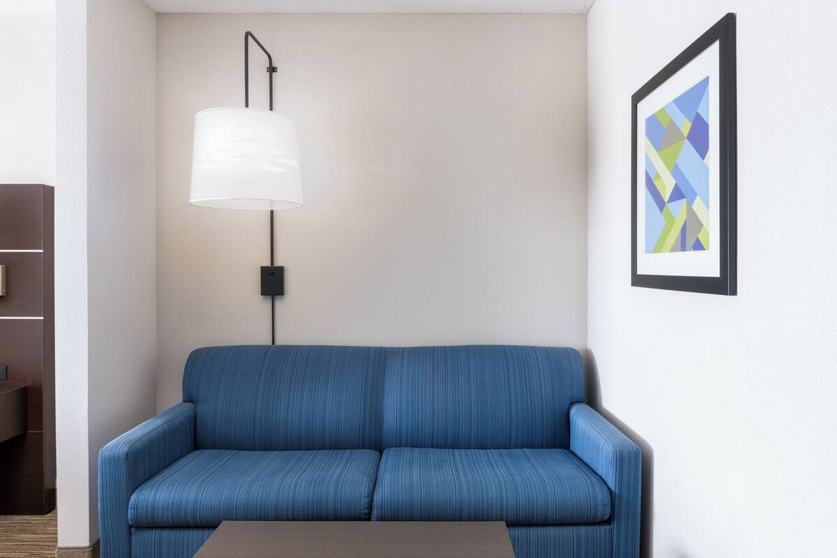 A blue sofa, a white floor lamp, and a framed abstract art piece on a white wall.