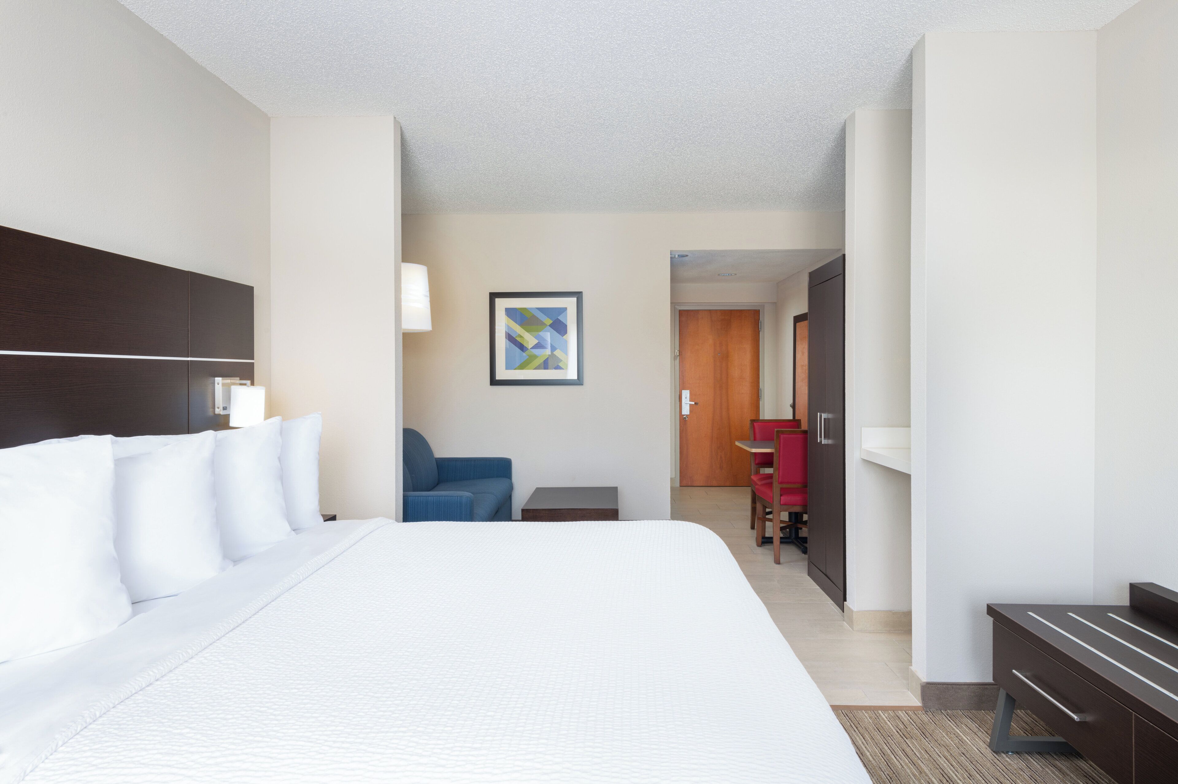 A hotel room with a large bed, a desk, a chair, and a door leading to another room.