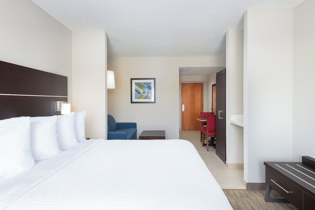 A hotel room with a large bed, a desk, a chair, and a door leading to another room.