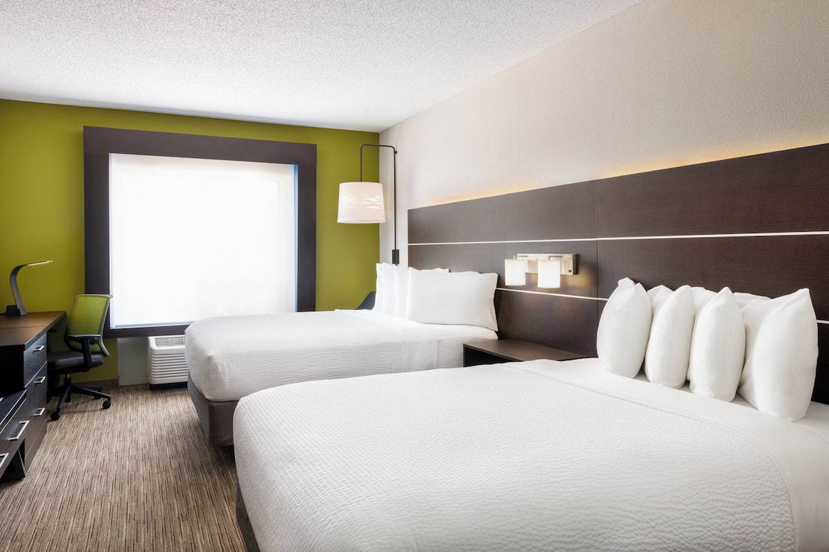 A hotel room with two beds, a desk, a chair, and a large window.