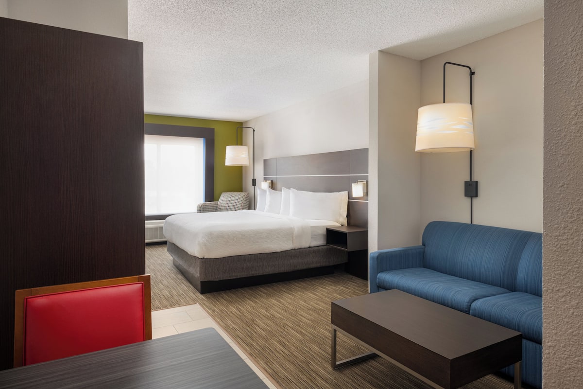 A hotel room with a bed, a sofa, a table, and a lamp.