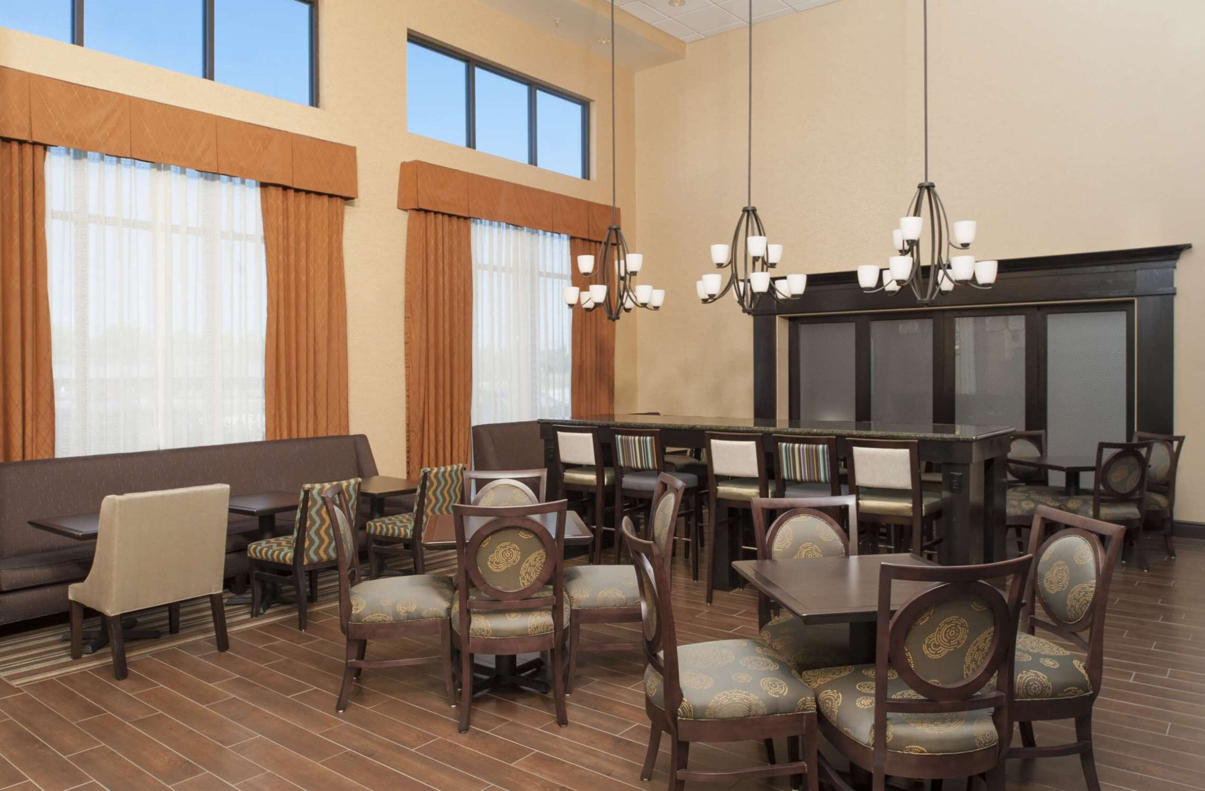 A spacious dining area with multiple tables and chairs, large windows with curtains, and a chandelier.