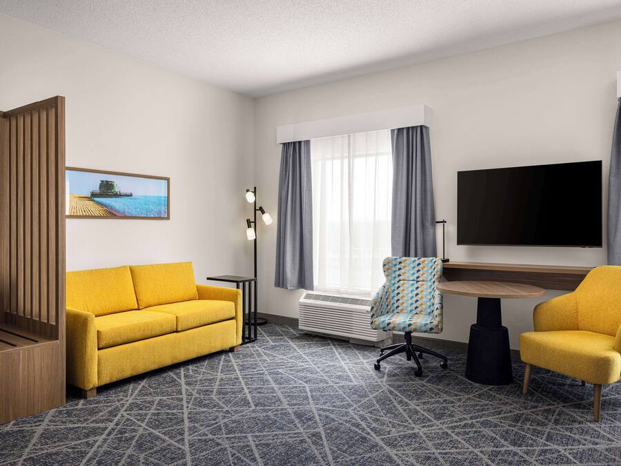 A hotel room with a yellow sofa, a small round table, a TV, and a window with curtains.