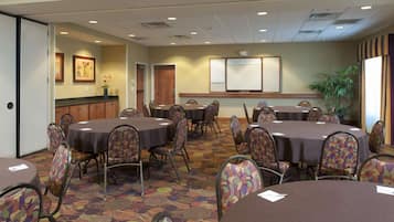 A conference room with round tables and chairs, a projector screen, framed pictures on the wall, and a potted plant.