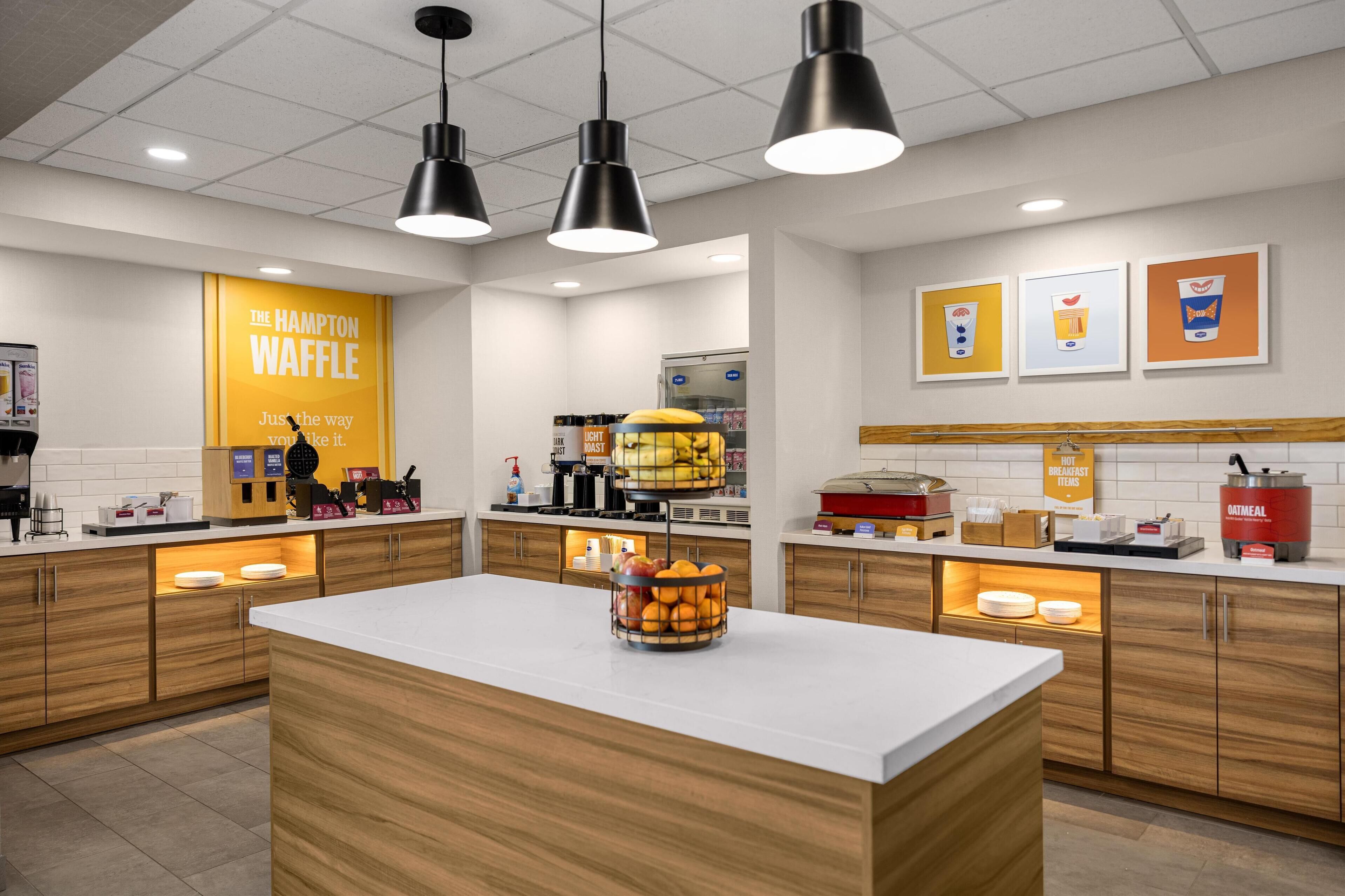Un área de cocina moderna con una isla central, armarios de madera e iluminación colgante.
