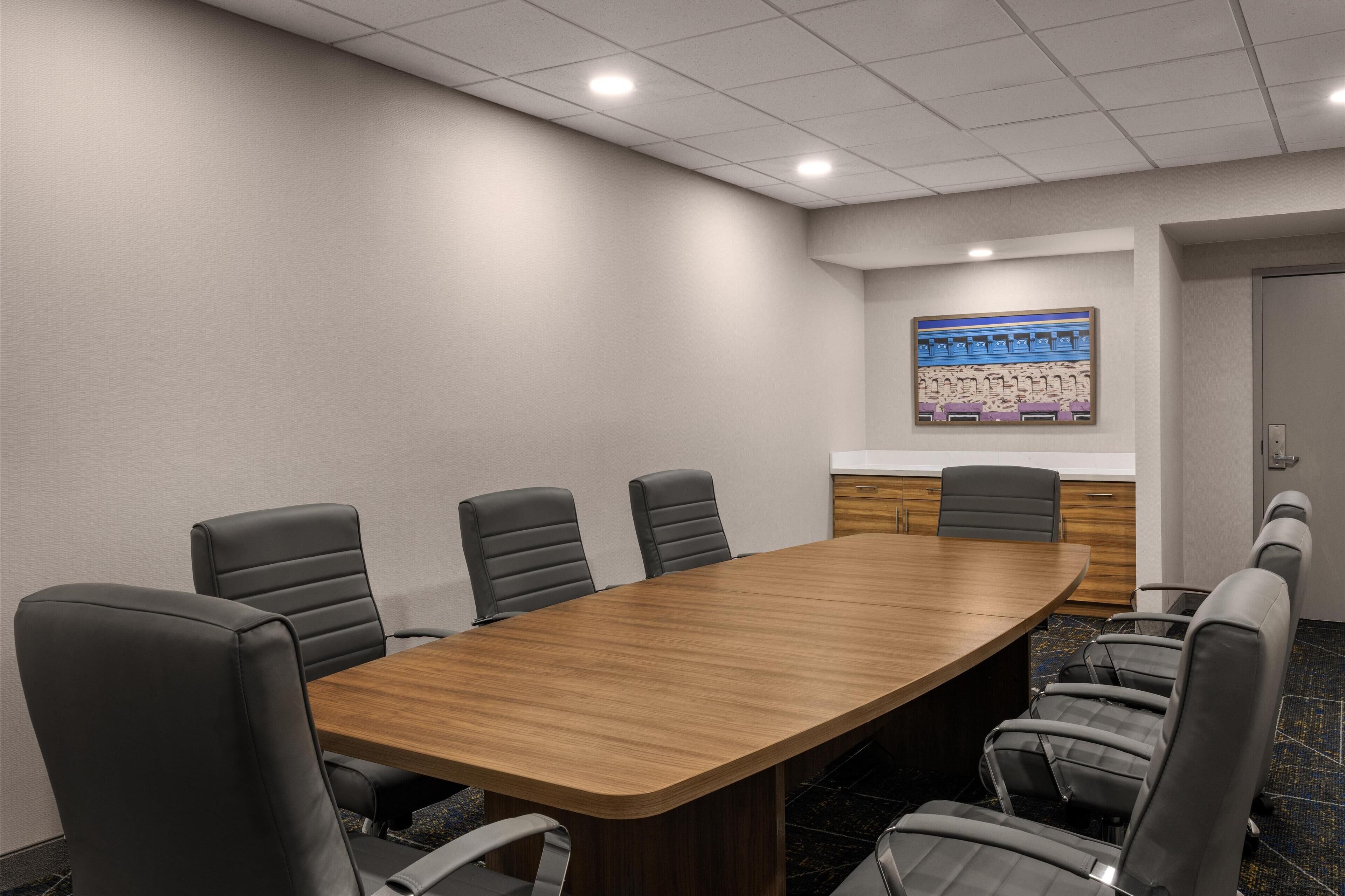 A conference room with a long wooden table, six black leather chairs, a whiteboard, and a door in the background.