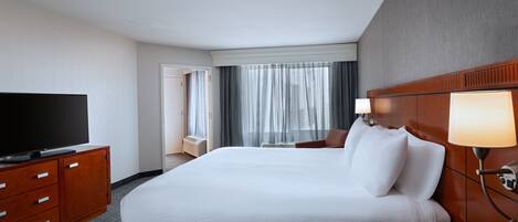 Une chambre d’hôtel avec un grand lit, un téléviseur à écran plat, une commode en bois et une table de chevet avec une lampe.
