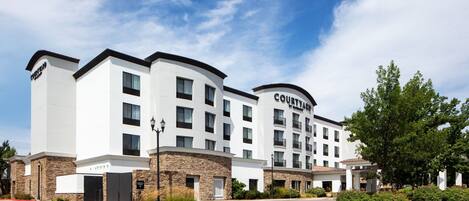 A Courtyard hotel with a modern design, featuring a flat roof, multiple balconies, and a central courtyard.