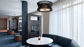 Un hall d’hôtel moderne avec une table ronde, un canapé en cuir noir et un téléviseur fixé sur un mur sombre.