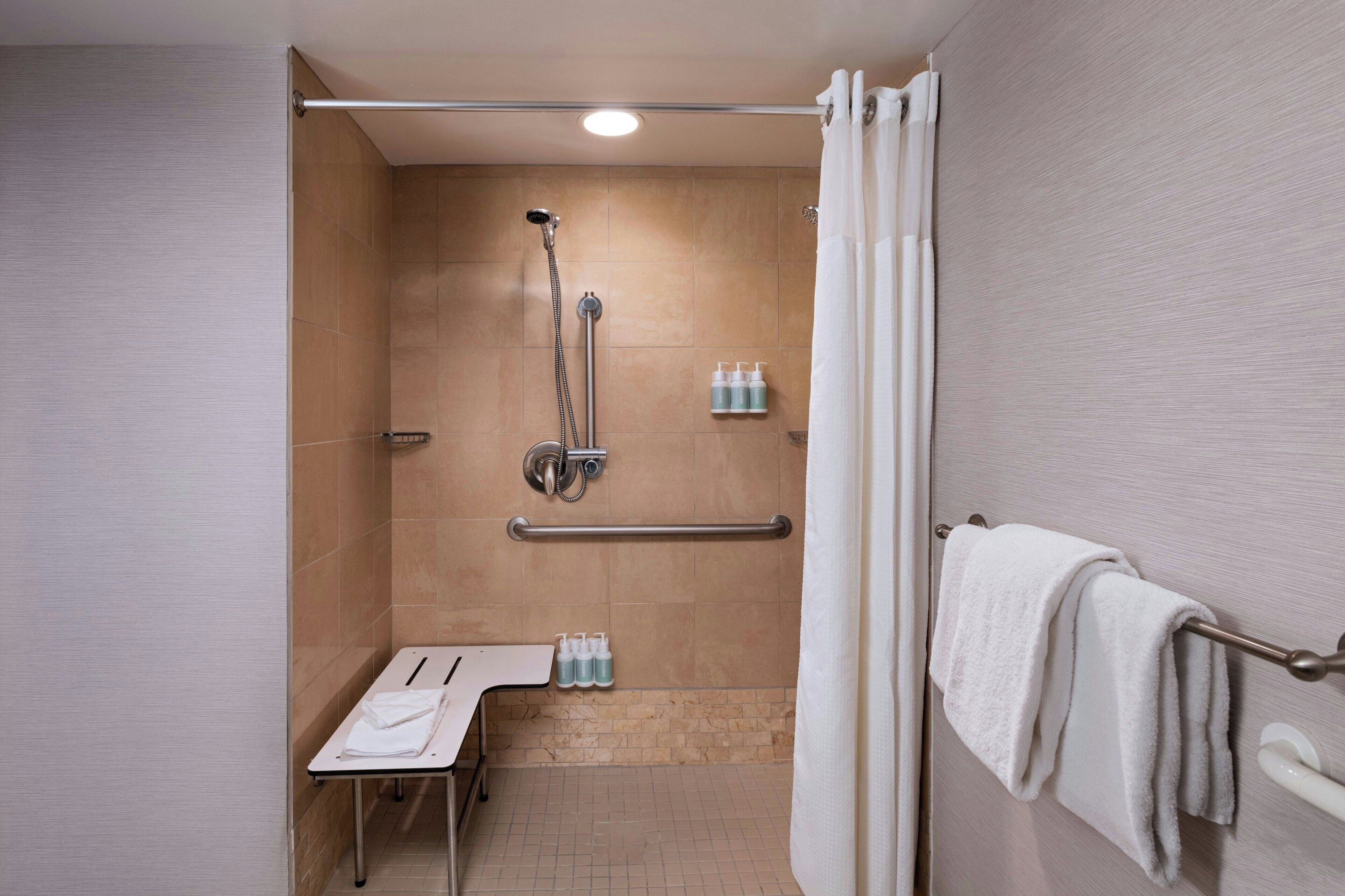 A modern bathroom with a shower, grab bars, a towel rack, and a bench.