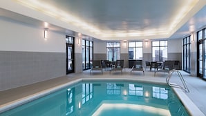 Une piscine intérieure offrant une vue dégagée sur le bassin, avec des murs carrelés et un espace détente comprenant des tables et des chaises.