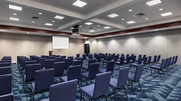 A conference room with rows of chairs, a projector screen, and a carpeted floor.