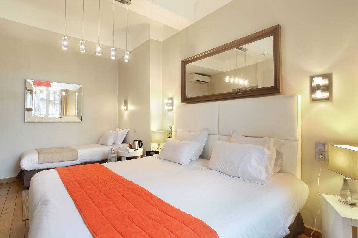 A hotel room with two beds, a large mirror, bedside lamps, and an air conditioning unit.