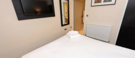 A hotel room with a bed, a flat-screen TV, a mirror, and a framed picture on the wall.
