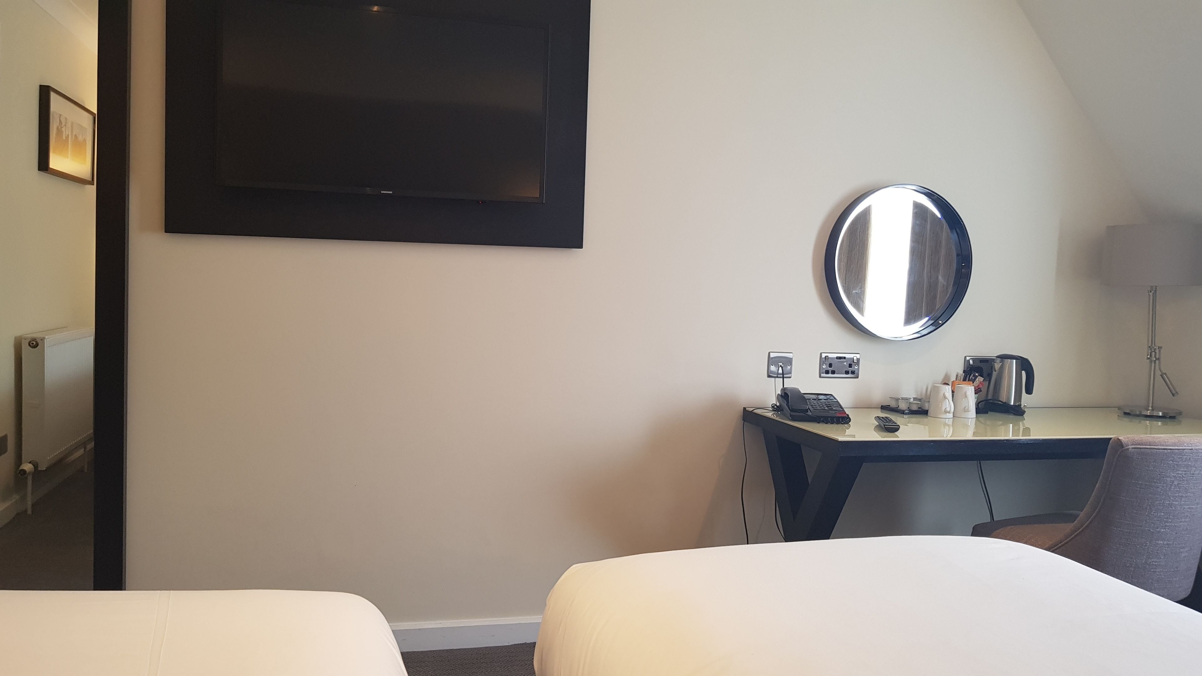 A hotel room with two beds, a desk with a telephone, a coffee maker, and a round mirror on the wall.