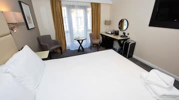 A hotel room with a large bed, a desk with a chair, a small table, a TV, and a window with curtains.