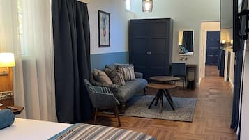 Habitación de hotel con cama, sofá, una mesita, armario y un pasillo que conduce a un baño.