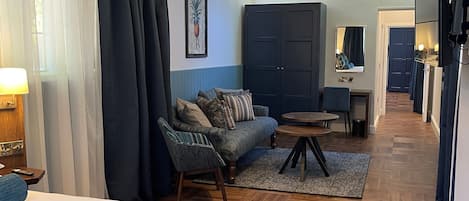 A hotel room with a bed, a sofa, a small table, a wardrobe, and a hallway leading to a bathroom.