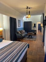 Habitación de hotel con cama, sofá, una mesita, armario y un pasillo que conduce a un baño.