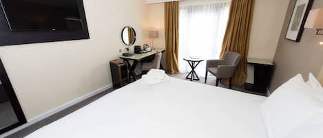 Habitación de hotel con una cama grande, un escritorio con silla, un televisor montado en la pared y una ventana con cortinas.