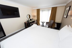 Habitación de hotel con una cama grande, un escritorio con silla, un televisor montado en la pared y una ventana con cortinas.