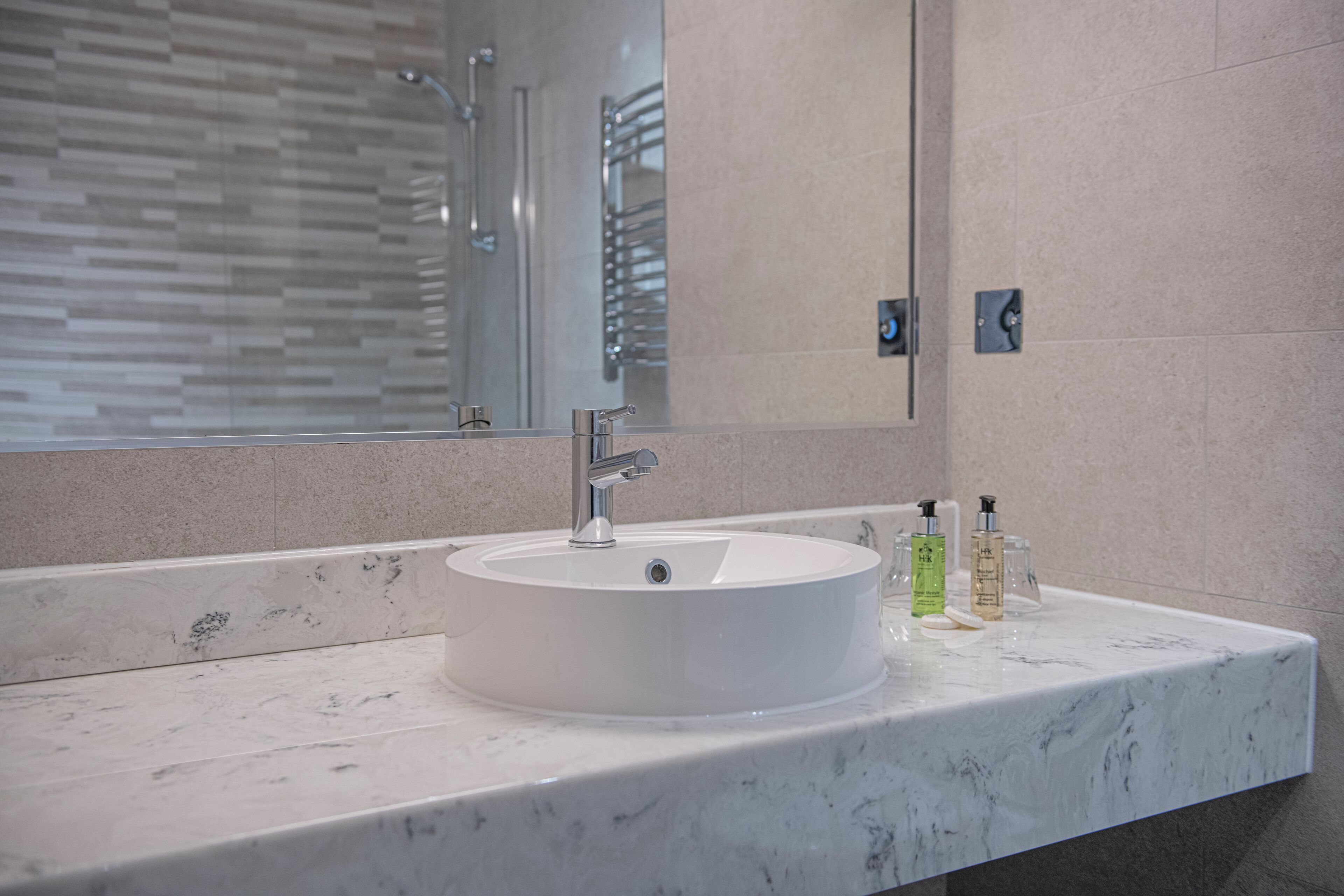 Un baño moderno con un lavamanos de mármol blanco, un espejo grande y un box de ducha de vidrio.