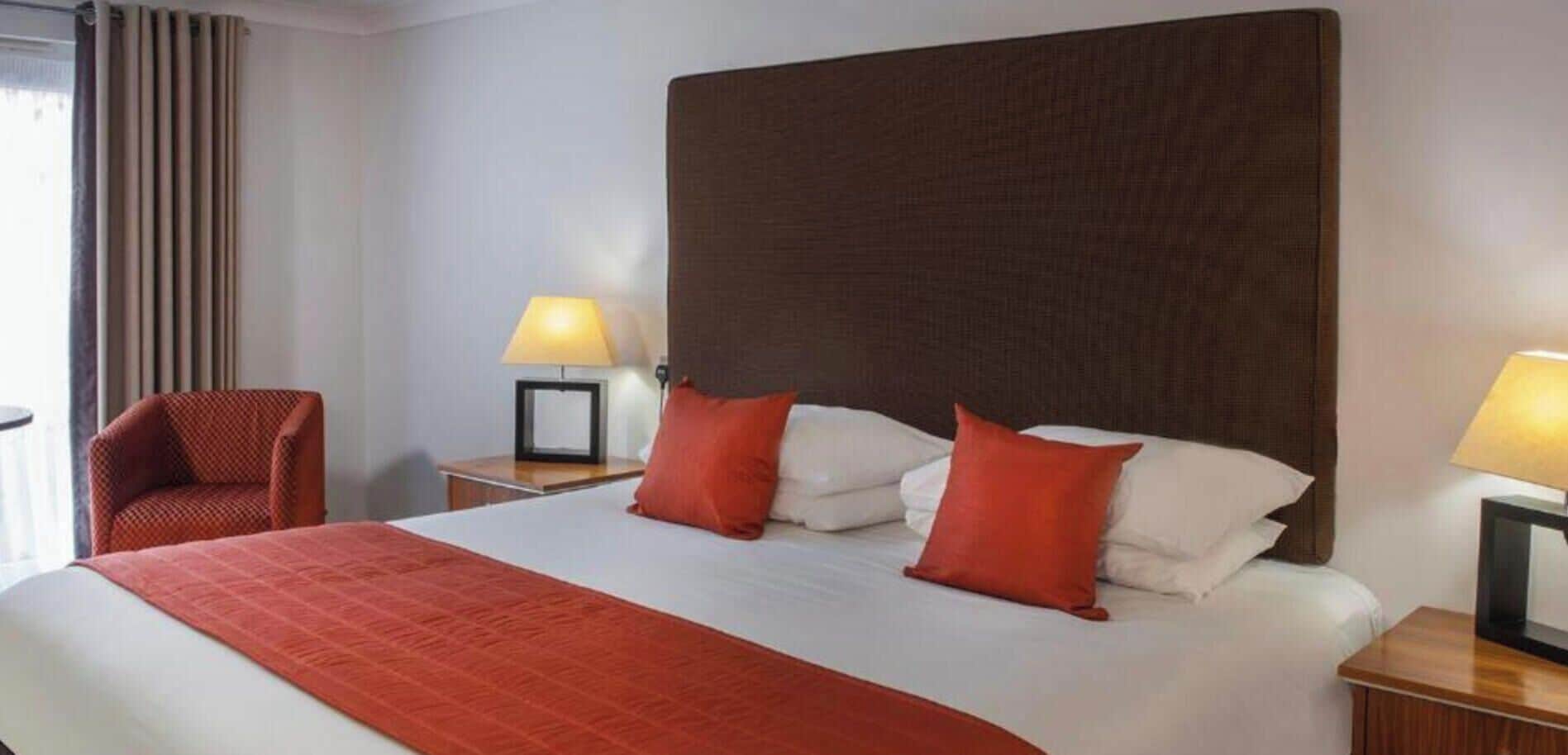 A hotel room with a large bed, two bedside tables, a chair, and a window with curtains.