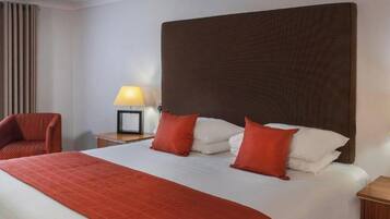A hotel room with a large bed, two bedside tables, a chair, and a window with curtains.
