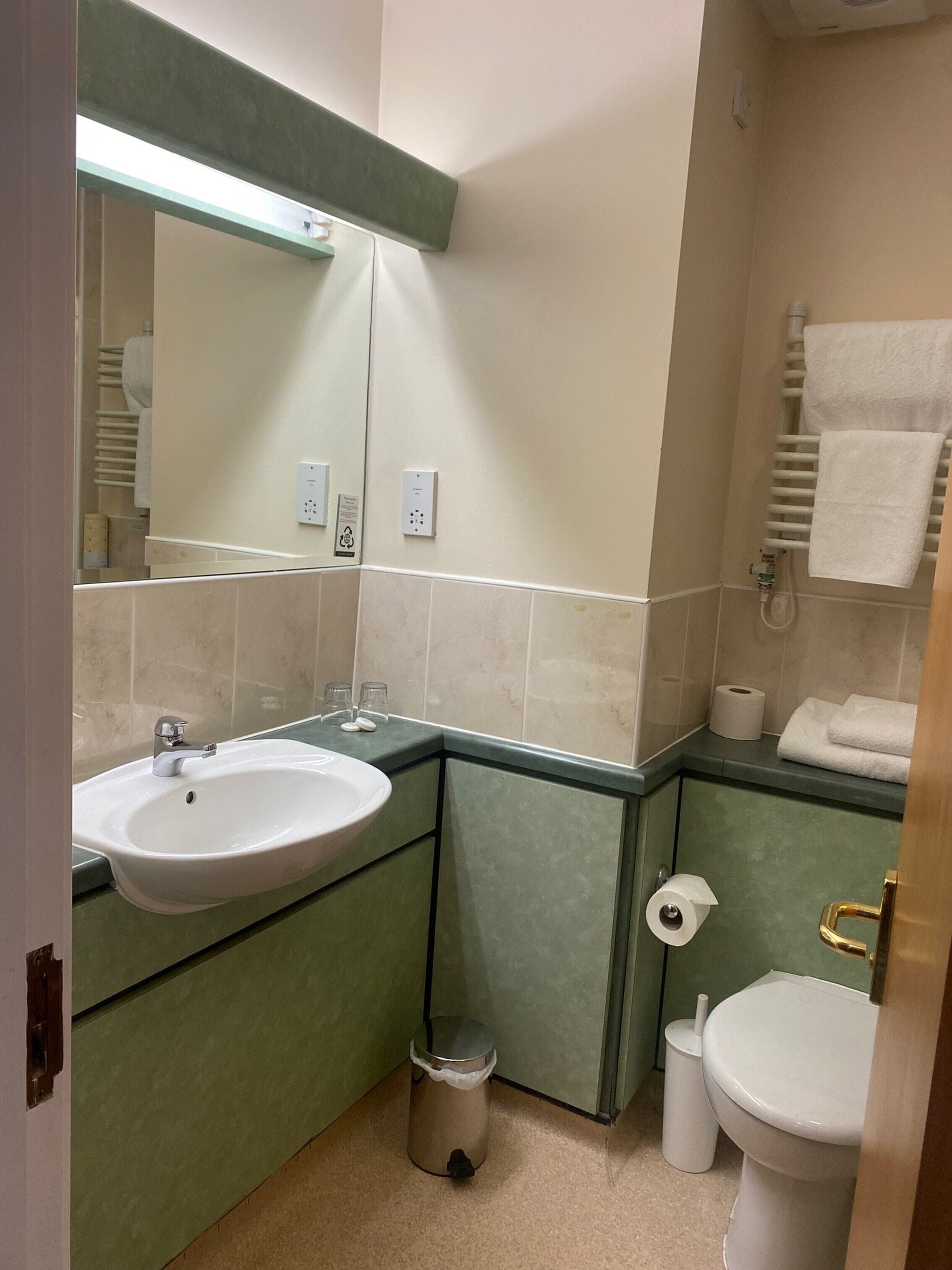 Un baño con lavamanos, espejo, inodoro y toallero.