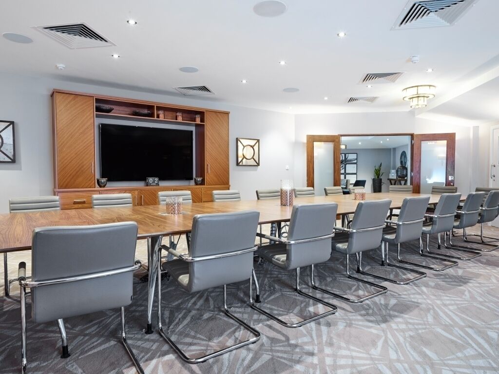 A conference room with a large table, multiple chairs, a television, and a modern ceiling design.