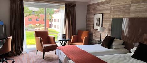 Una habitación de hotel con una cama, dos sillones, un escritorio y vistas a un patio.