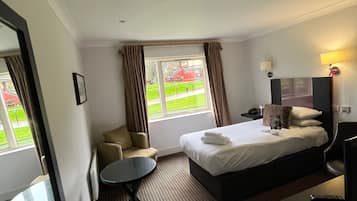 Habitación de hotel con cama, una pequeña mesa, una silla, un sofá y una ventana con cortinas.