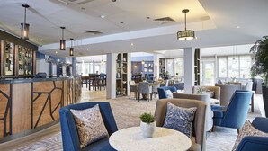 A modern hotel lobby with seating areas, a bar, and a dining space. - Staverton Park Hotel & Golf Club (Daventry)
