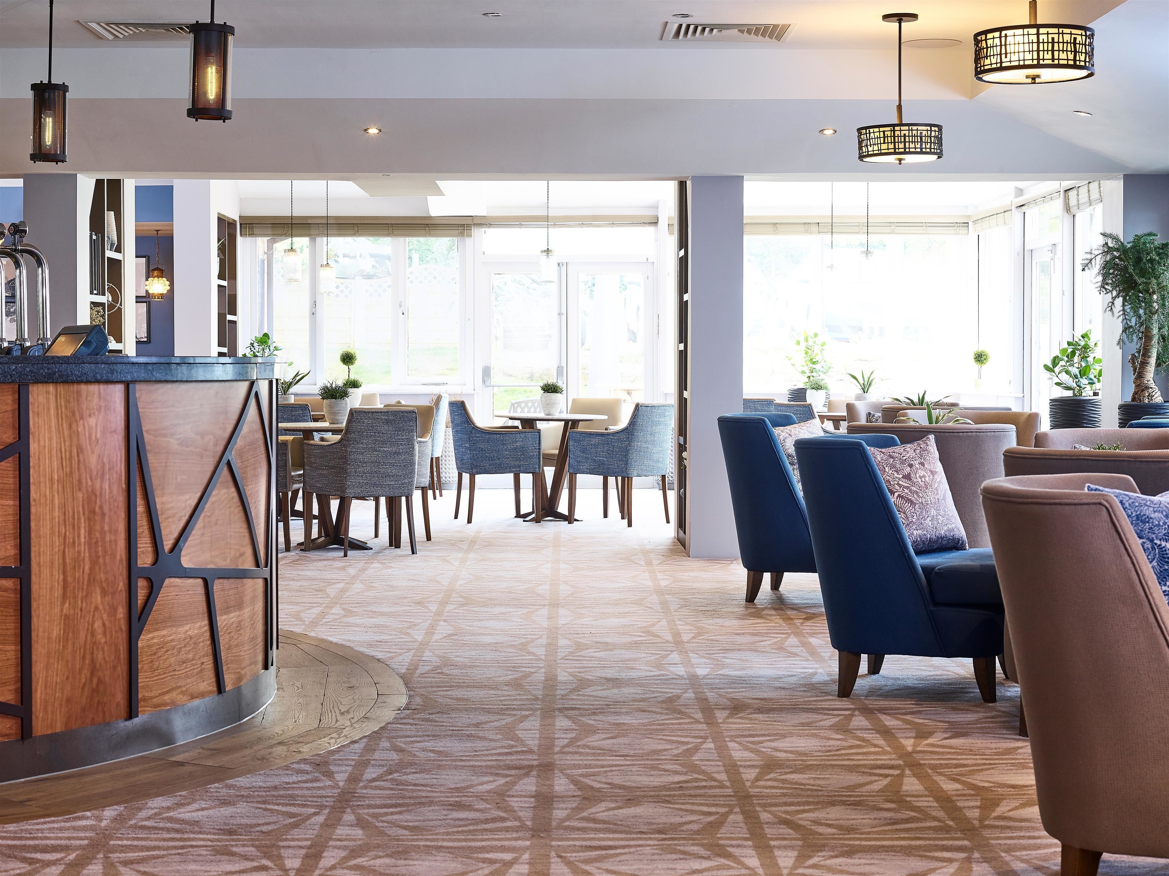 A modern interior with a bar area, seating with blue and brown chairs, and large windows allowing natural light.