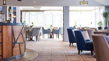 A modern interior with a bar area, seating with blue and brown chairs, and large windows allowing natural light.