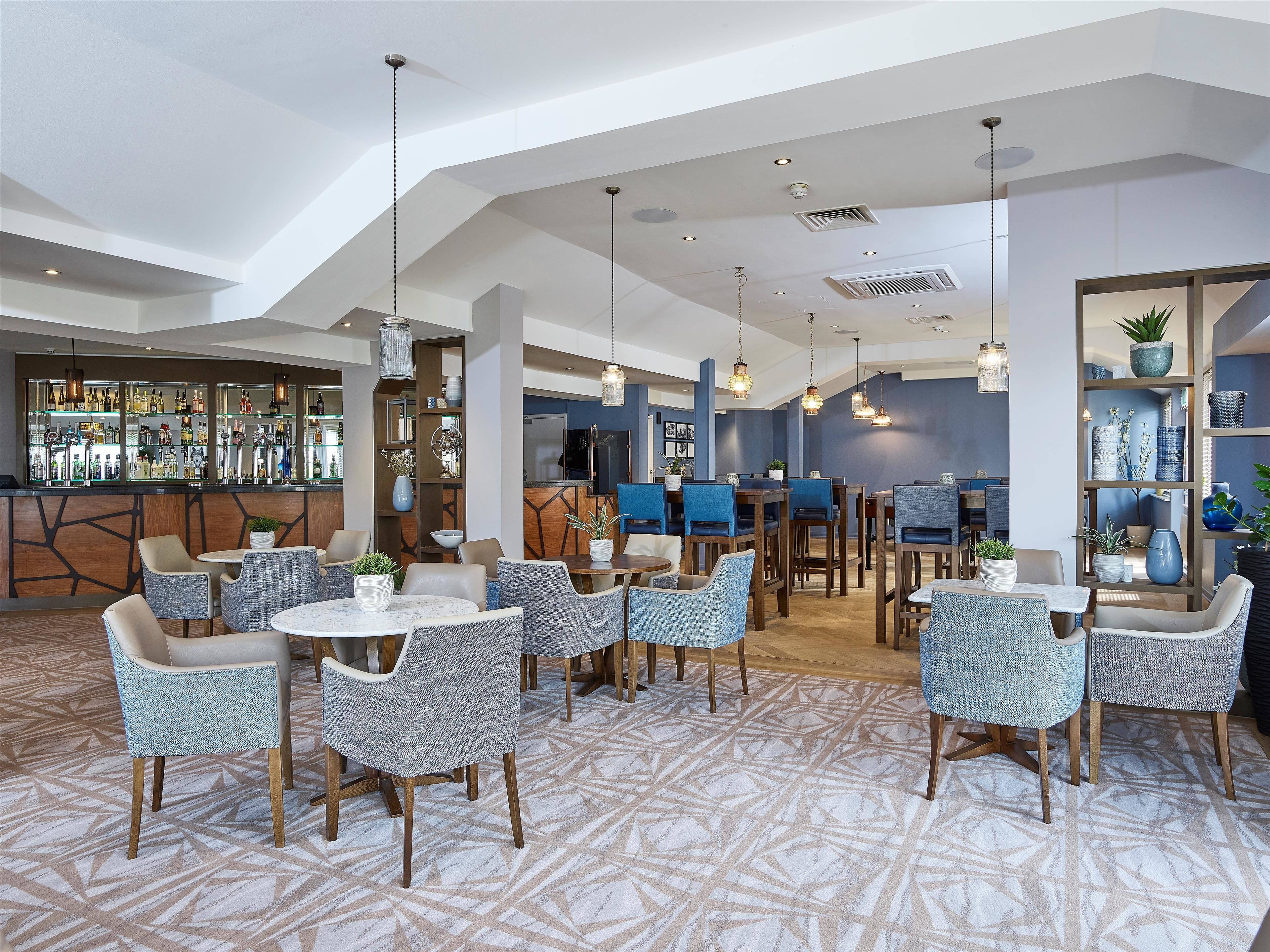 A modern hotel lobby with a bar area, seating arrangements, and a patterned carpet.