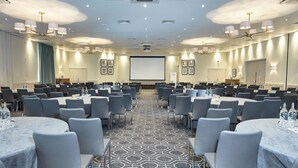 A conference room with multiple tables and chairs, a projector screen, and a patterned carpet. - Staverton Park Hotel & Golf Club (Daventry)