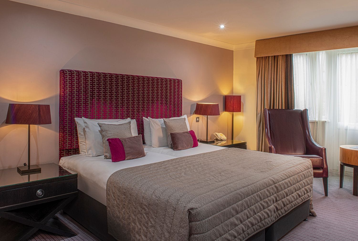 Una habitación de hotel con una cama grande, dos mesitas de noche con lámparas, una silla y una pequeña mesa.