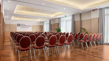 Un salón de conferencias con filas de sillas rojas, un cartel de Hilton Garden Inn y suelo de madera.