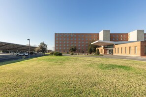 A Hilton Garden Inn with a large parking lot, a grassy area, and a clear blue sky.