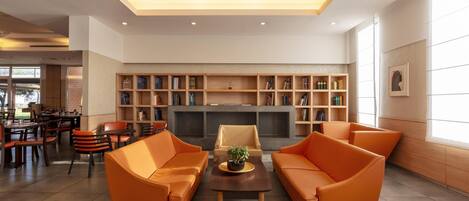 A modern lounge area with orange sofas, a fireplace, and a bookshelf.
