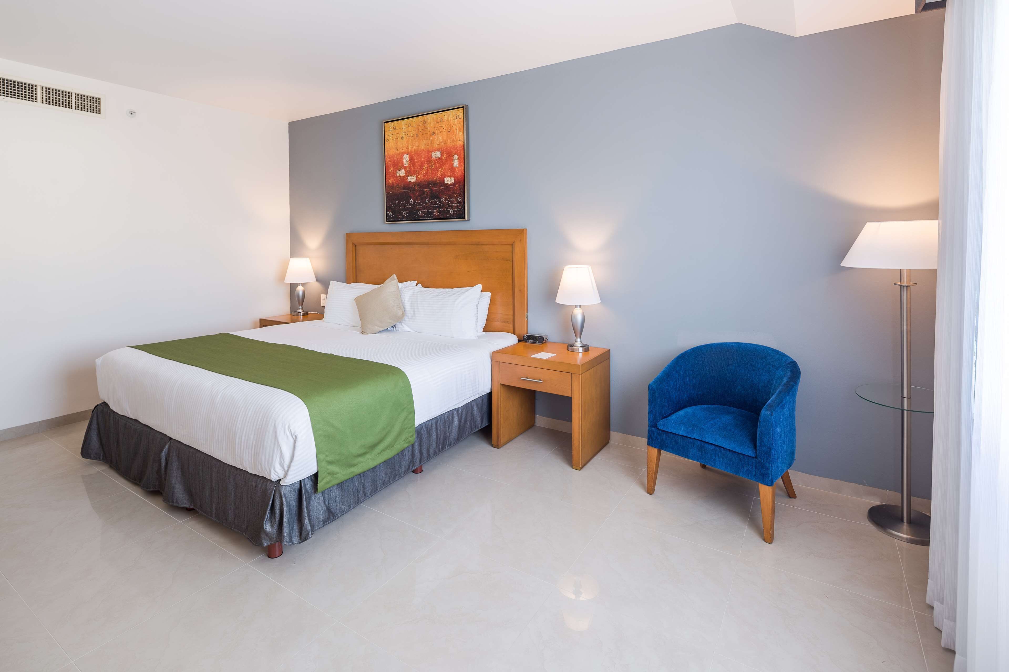 A hotel room with a bed, two bedside tables with lamps, a blue chair, and a floor lamp.