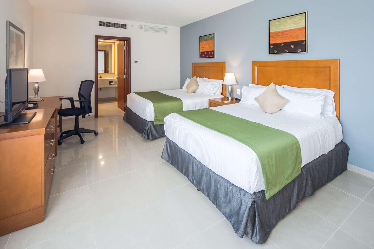 A hotel room with two beds, a desk with a computer, and a chair.