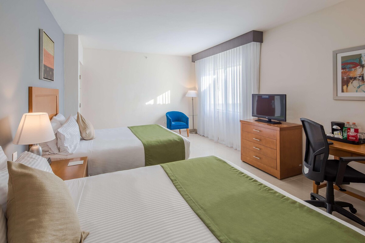 A hotel room with two beds, a desk with a computer, a chair, a television, and a wardrobe.