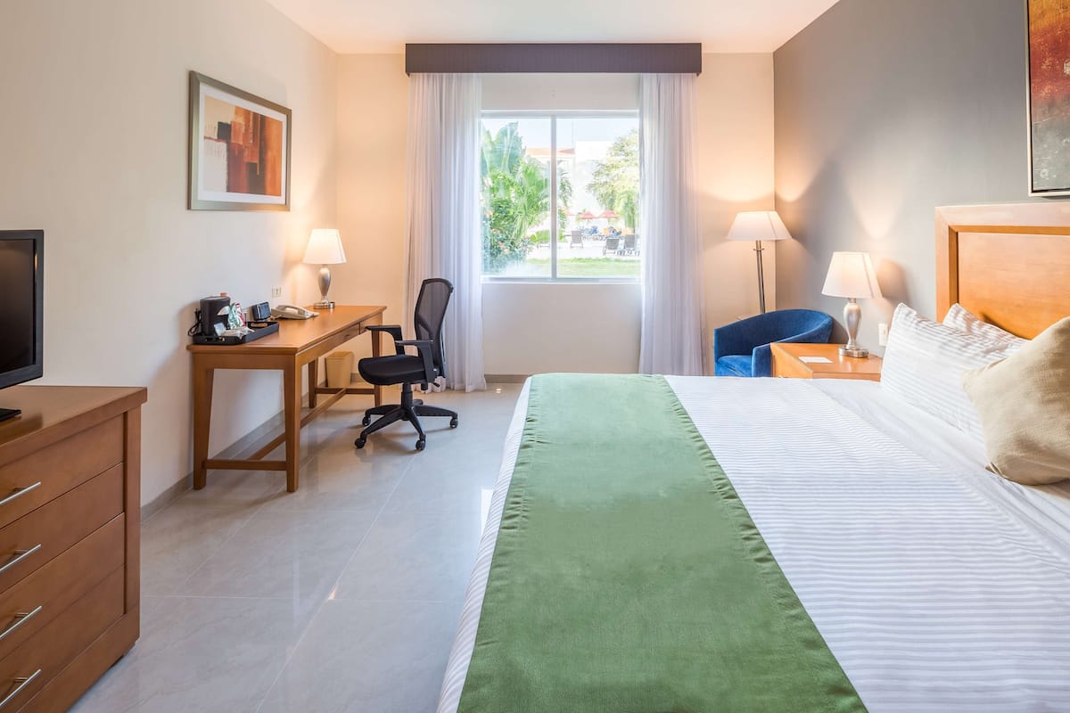 A hotel room with a bed, desk, chair, TV, and a window with curtains.